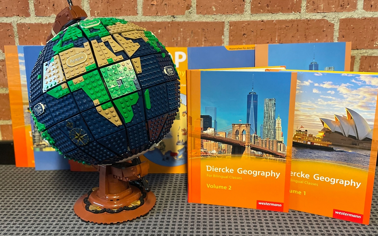 Mehrere Schulbücher für bilingualen Sachunterricht stehen mit einem Lego-Globus auf dem Boden