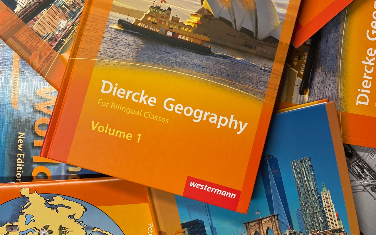 Mehrere Schulbücher für bilingualen Sachunterricht liegen gefächert übereinander