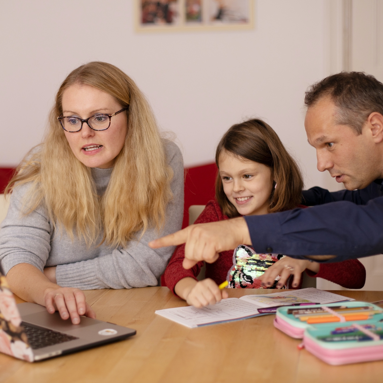 Eltern sitzen mit ihrer Tochter am Küchentisch und erledigen Schularbeit